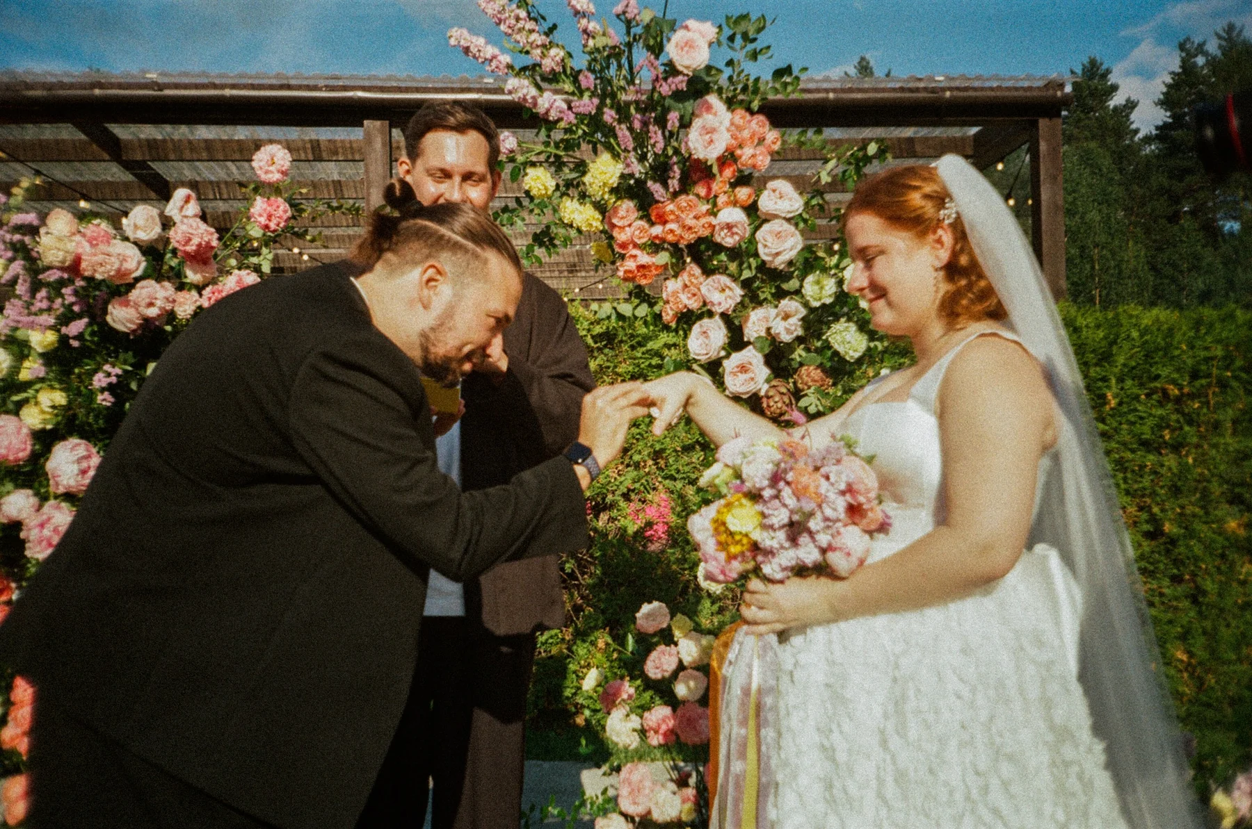 Film photograph of the groom placing a ring on the bride's hand during the same outdoor ceremony
