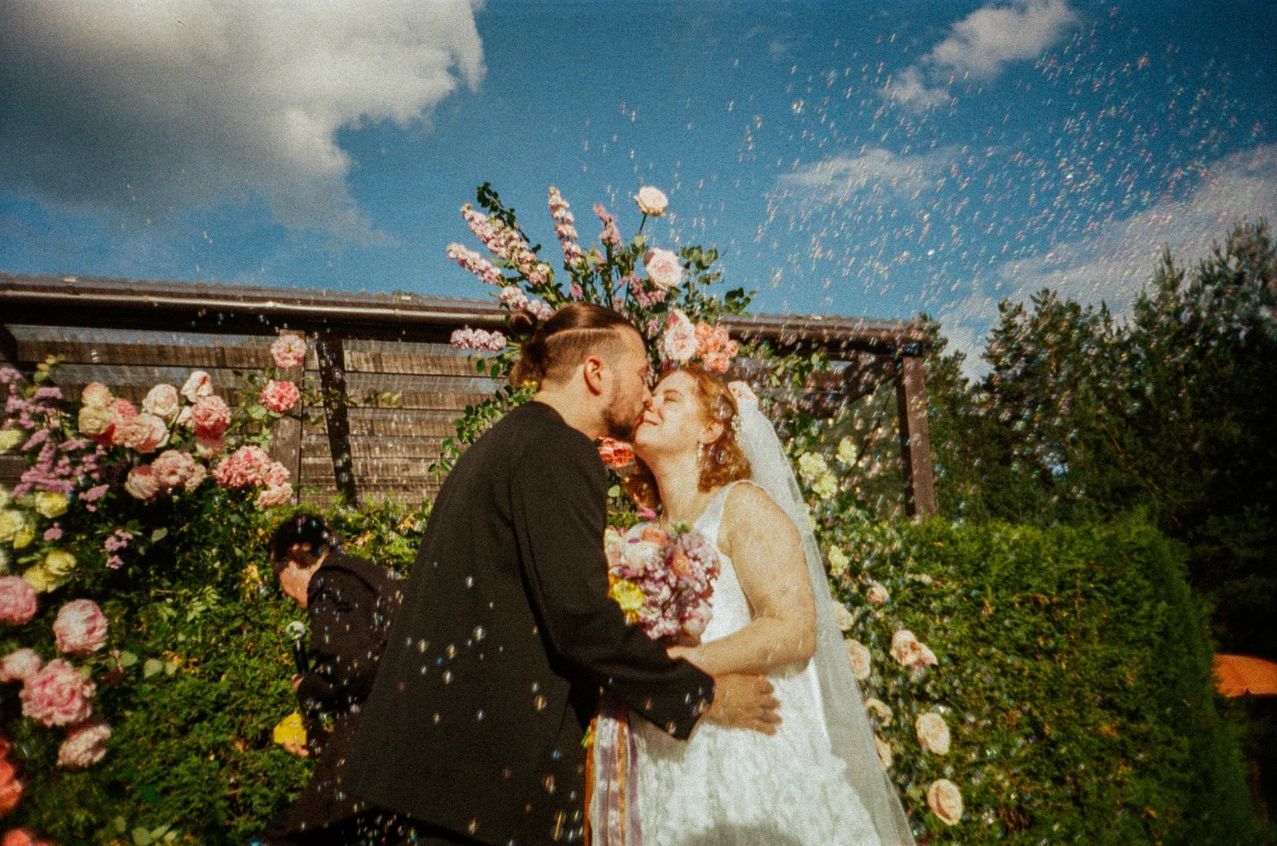 Newlyweds kissing beneath falling confetti in a photograph made on film