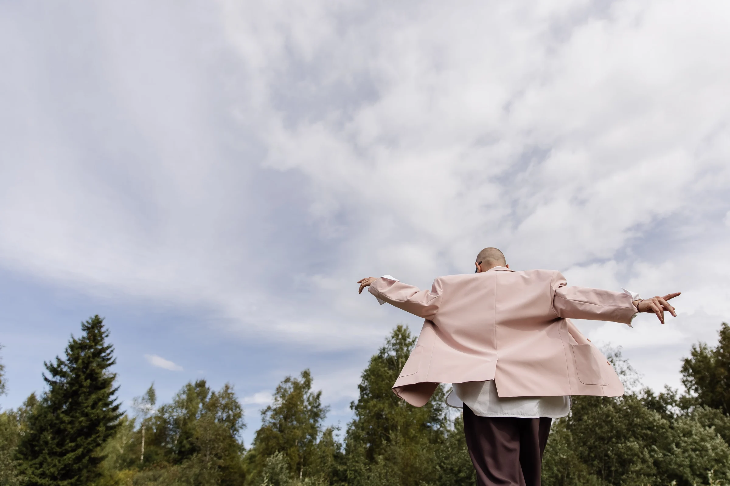 A man in a pink jacket with his arms outstretched beneath an open sky