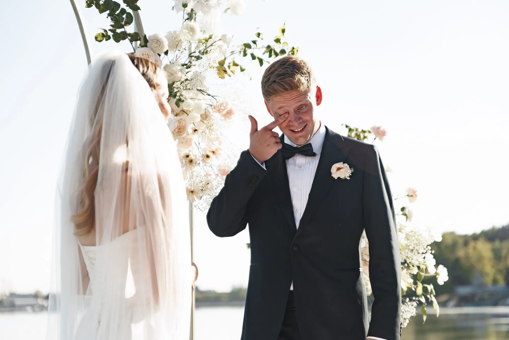 Egor wiping a tear while facing Ekaterina under their outdoor ceremony arch